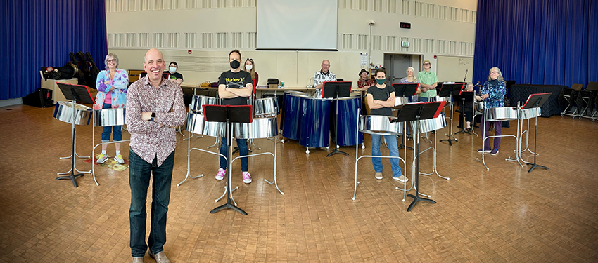 Dr William Dyer standing in front of a group of people playing steel drums